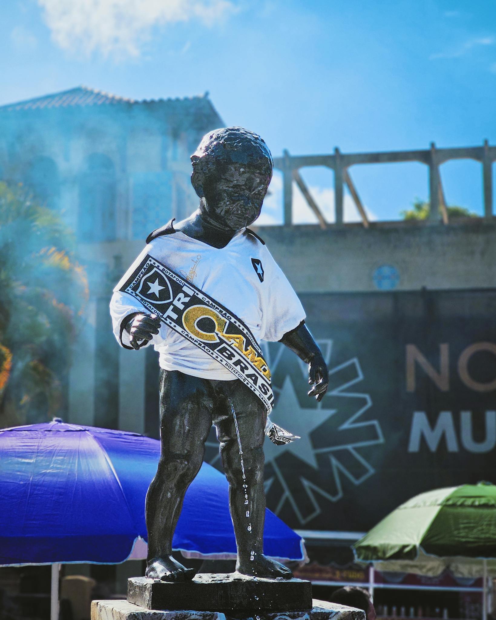 A statue of a child wearing a soccer jersey displayed at an outdoor event on a sunny day.